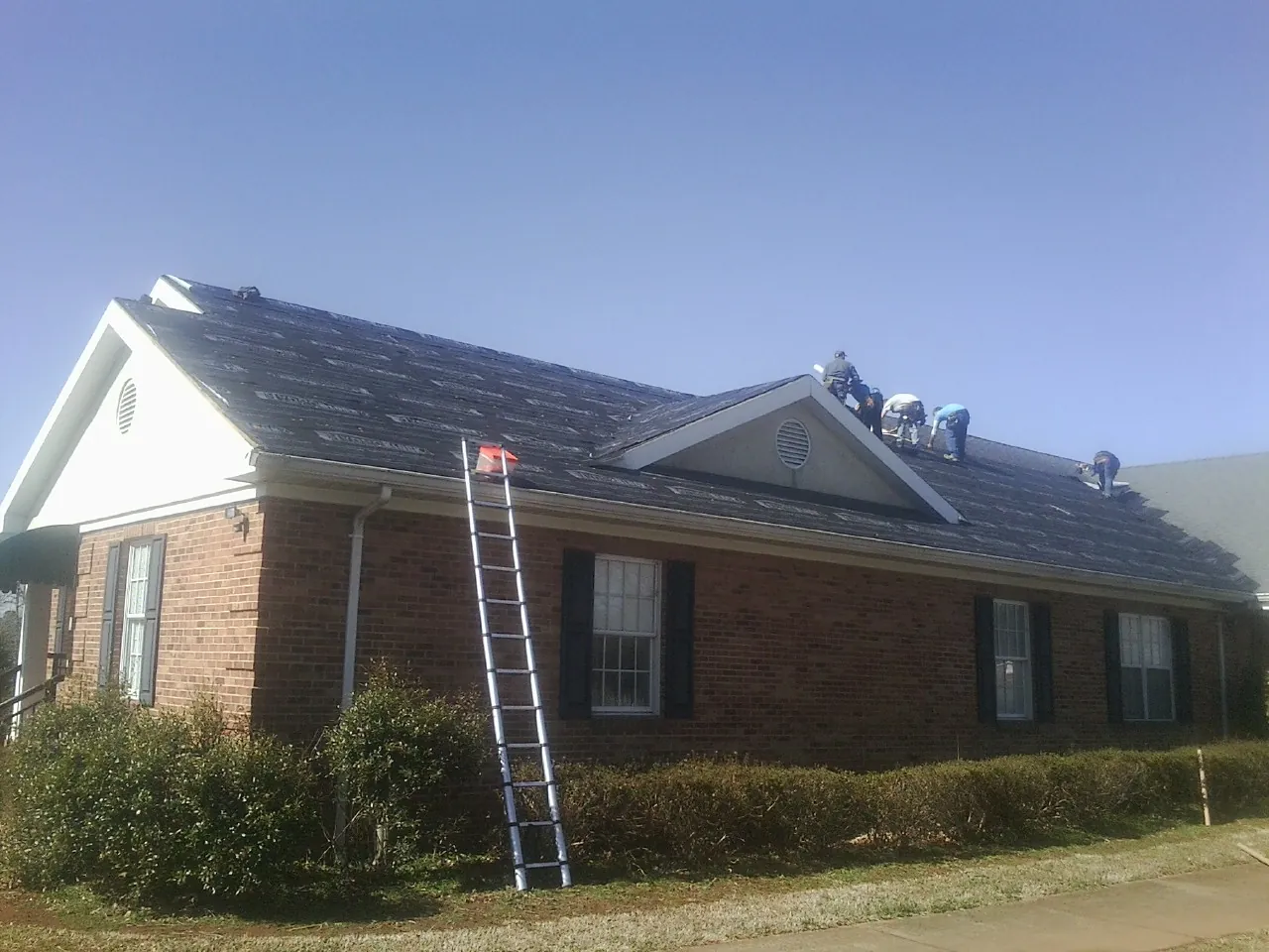 Crew tearing shingles off a brick ranch roof with a ladder set — Emergency Roof Repair work by our crew in Yantic