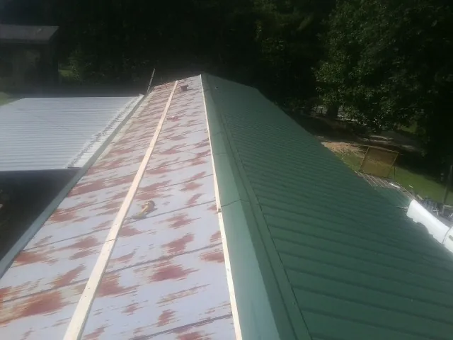 Old rusted panels beside newly installed green metal roofing — Wind Damage Roof Repair by Roofing Brothers in Yantic